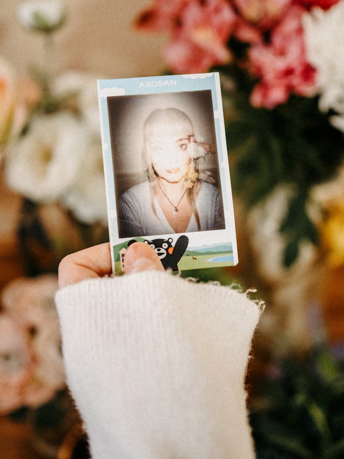 Close-up of a hand in a knitted sweater holding a Polaroid photo against a blurred floral background.