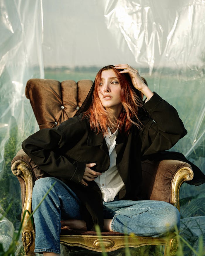 Woman with red hair in casual attire sitting on an outdoor vintage chair.